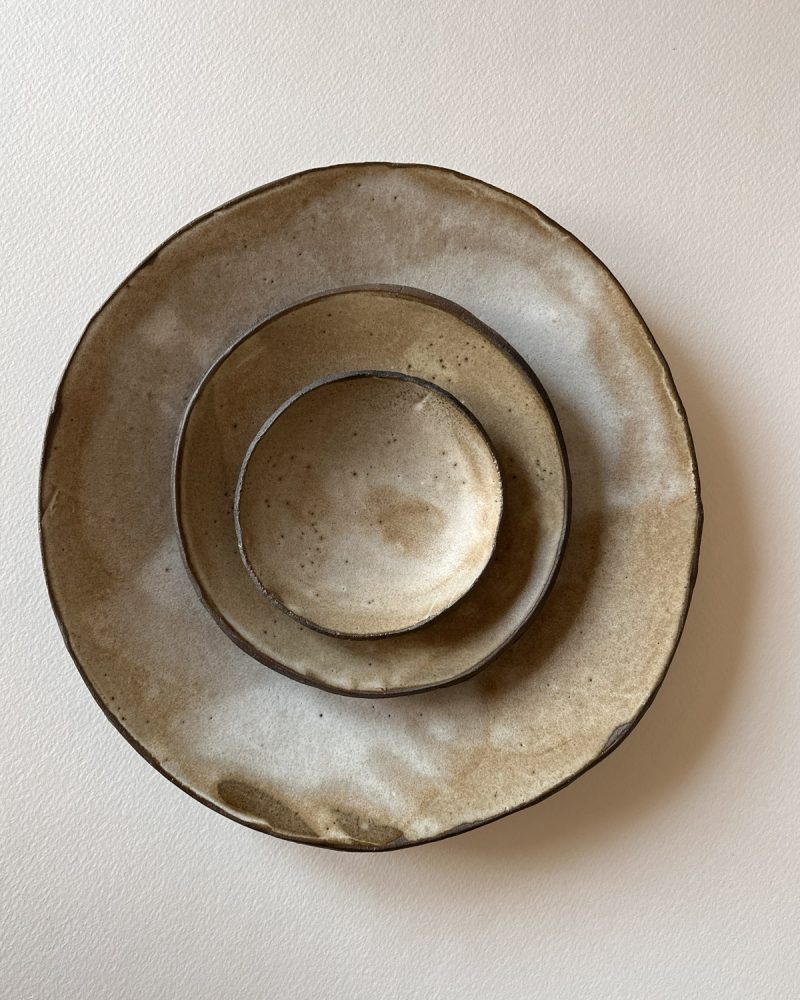 Assiette, petite assiette et coupelle en grès brun émaillé beige empilées, vues de dessus