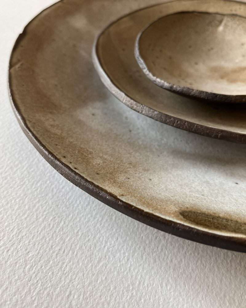 Gros plan sur les bords irréguliers d'assiettes en grès brun à l'émail beige nuageux empilées