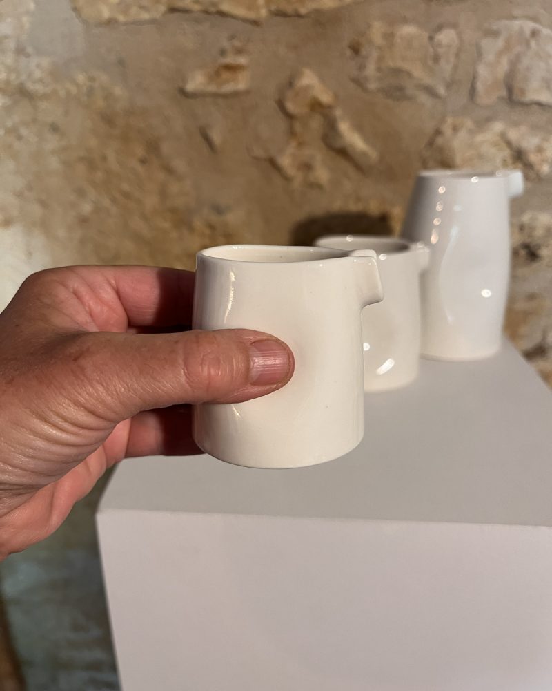 Main tenant une saucière verseuse en porcelaine blanche devant les autres tailles, sur socle