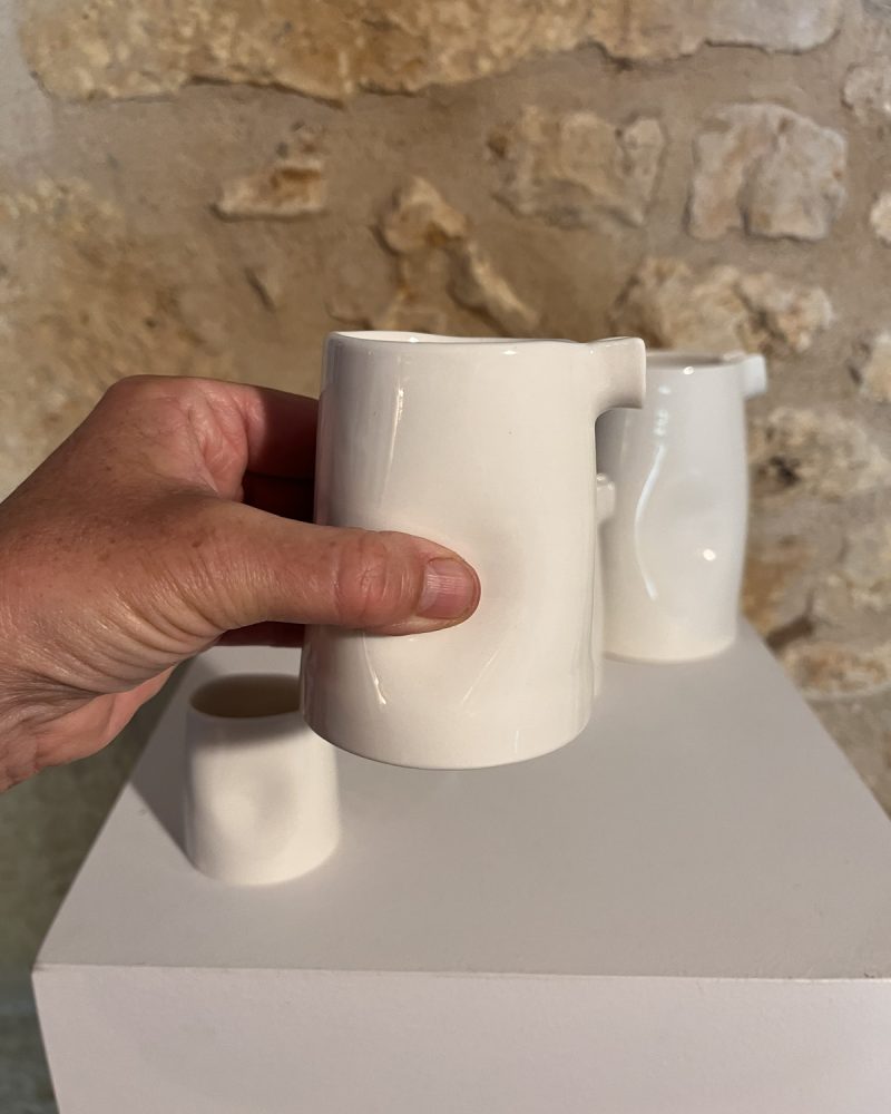 Main tenant le grand modèle de la saucière verseuse en porcelaine blanche, petits modèles derrière