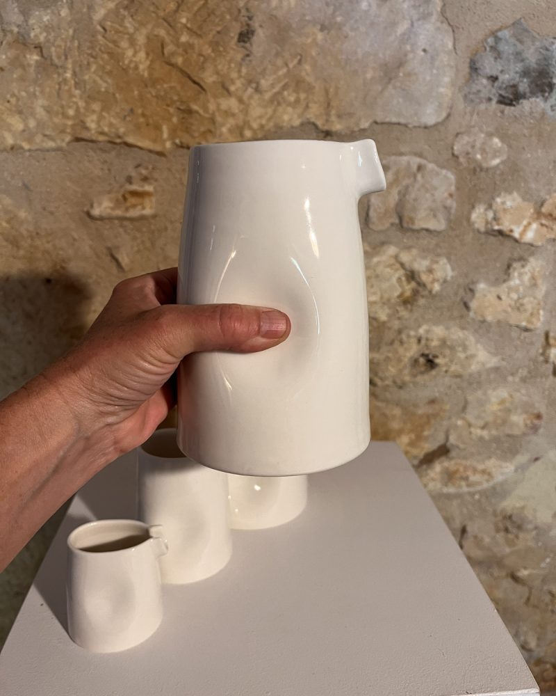 Main saisissant la grande saucière verseuse en porcelaine blanche par son renfoncement, sur socle