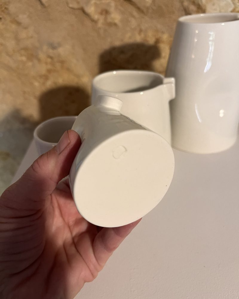 Dessous d'une saucière verseuse en porcelaine blanche tenue en main, tampon visible, autres saucières derrière