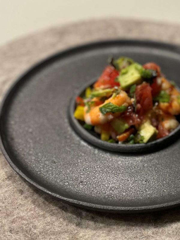Coupelle en grès noir posée sur une assiette texturée noire, garnie d'un tartare de légumes