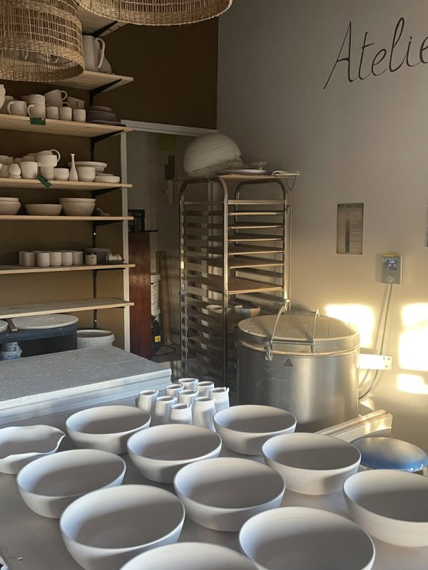 Atelier de céramique avec bols et gobelets en séchage sur la table, étagères de pièces et four
