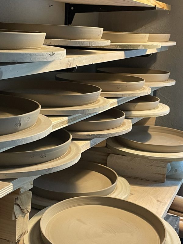 Assiettes et plats en terre crue posés sur des planches de séchage dans l'atelier