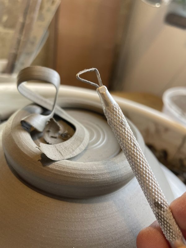 Mirette affinant le pied d'un bol en argile retourné sur le tour, copeaux d'argile