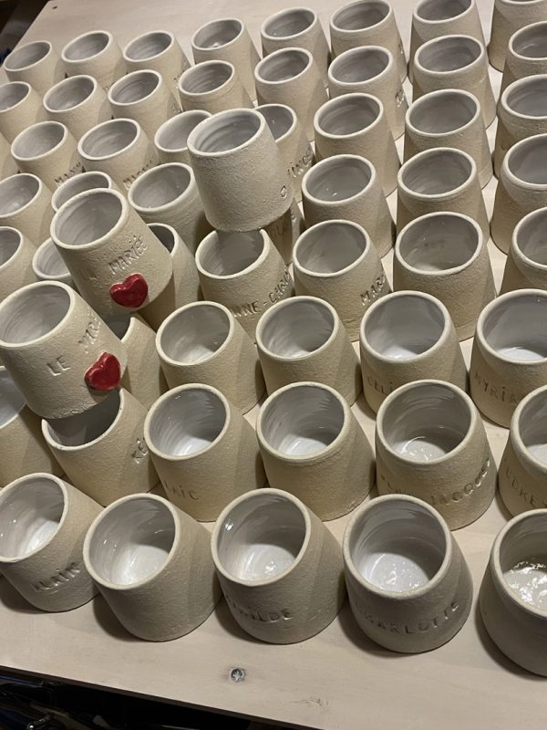 Dizaines de gobelets en grès gris marqués d'initiales, alignés sur une planche, cadeaux d'invités de mariage