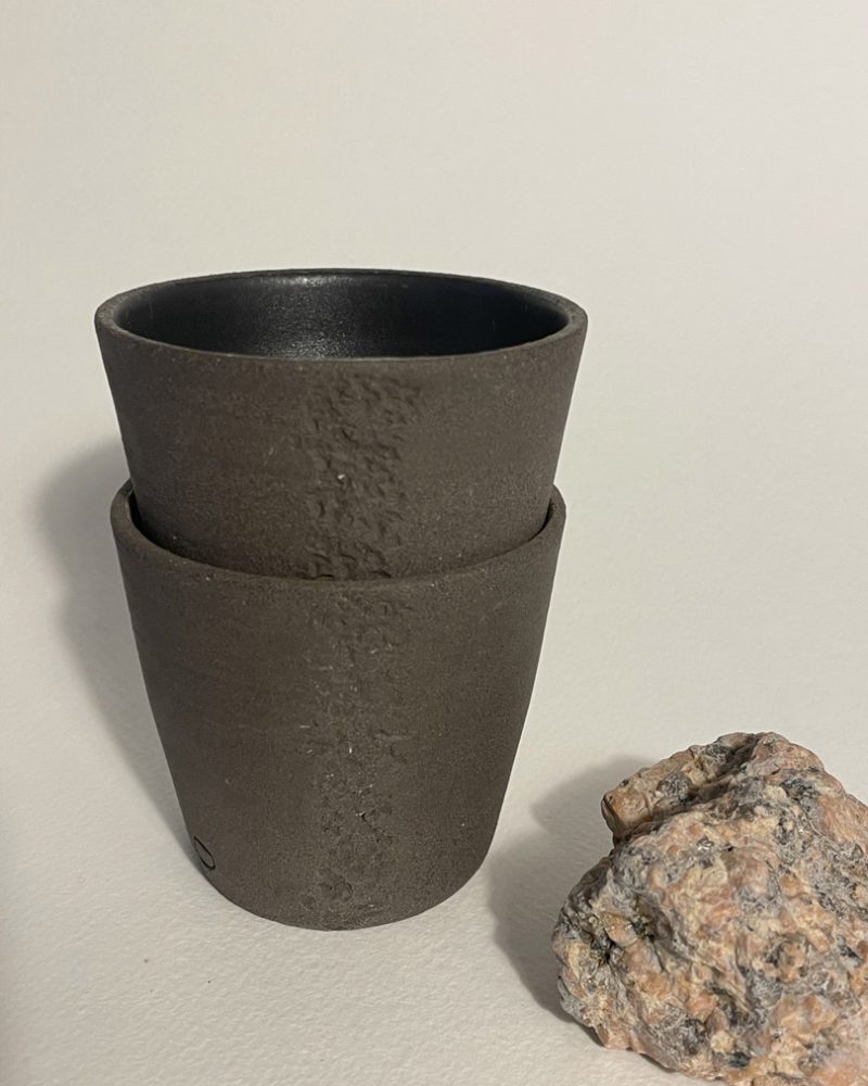 Gobelets Treb empilés avec granit rose Deux gobelets Treb en grès brun brut empilés, intérieur noir mat, morceau de granit rose